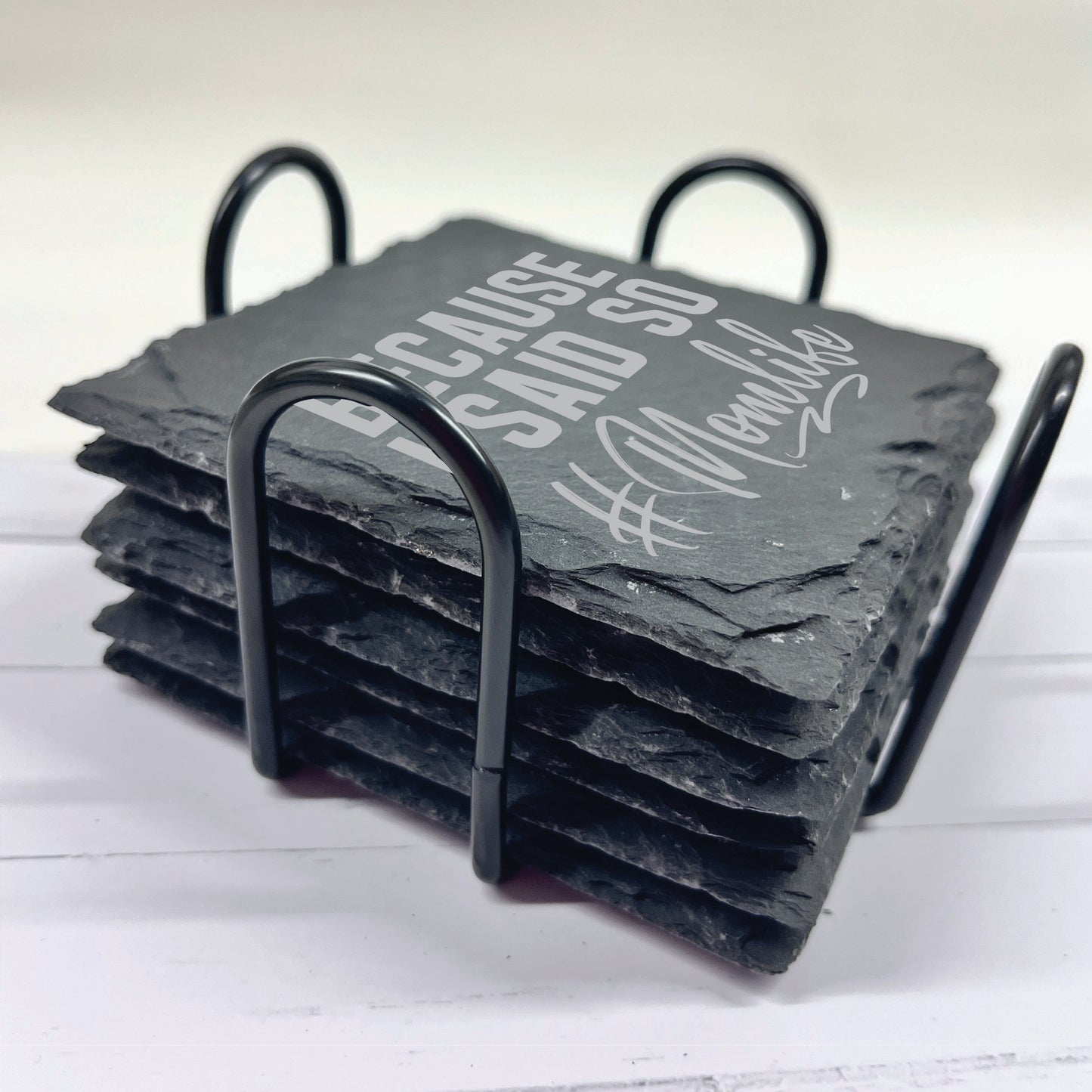 Set of slate coasters with text in a black holder on a white surface