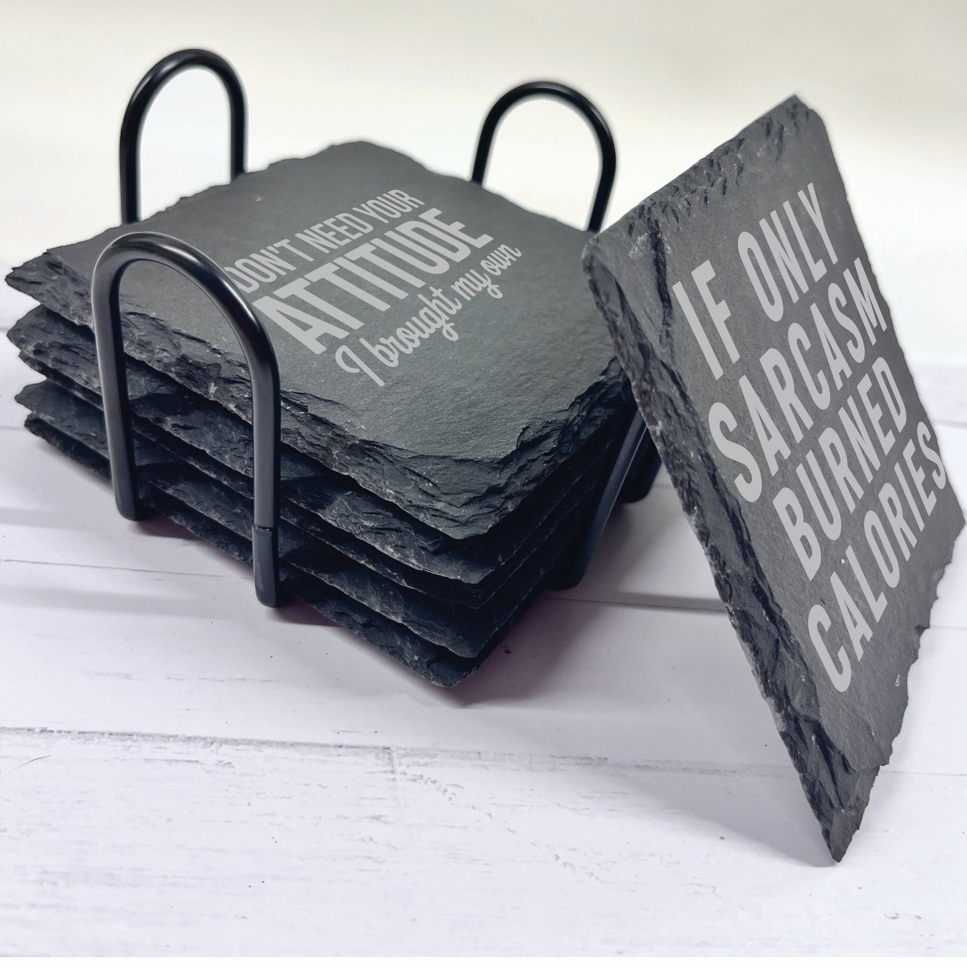 Set of slate coasters with humorous sayings on a black metal rack.