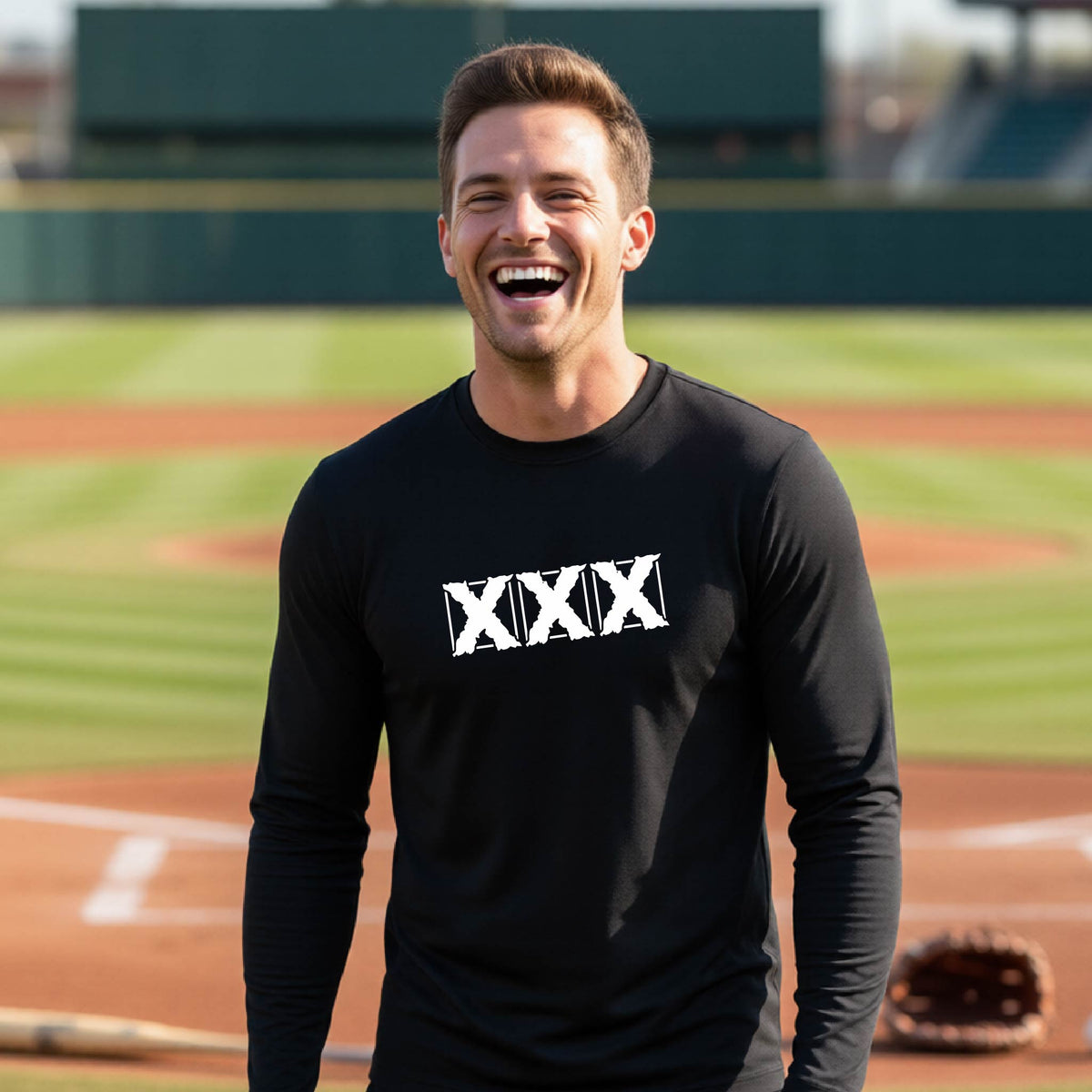 A man laughing on a baseball field wearing a black long-sleeve t-shirt with a white XXX logo across the chest.