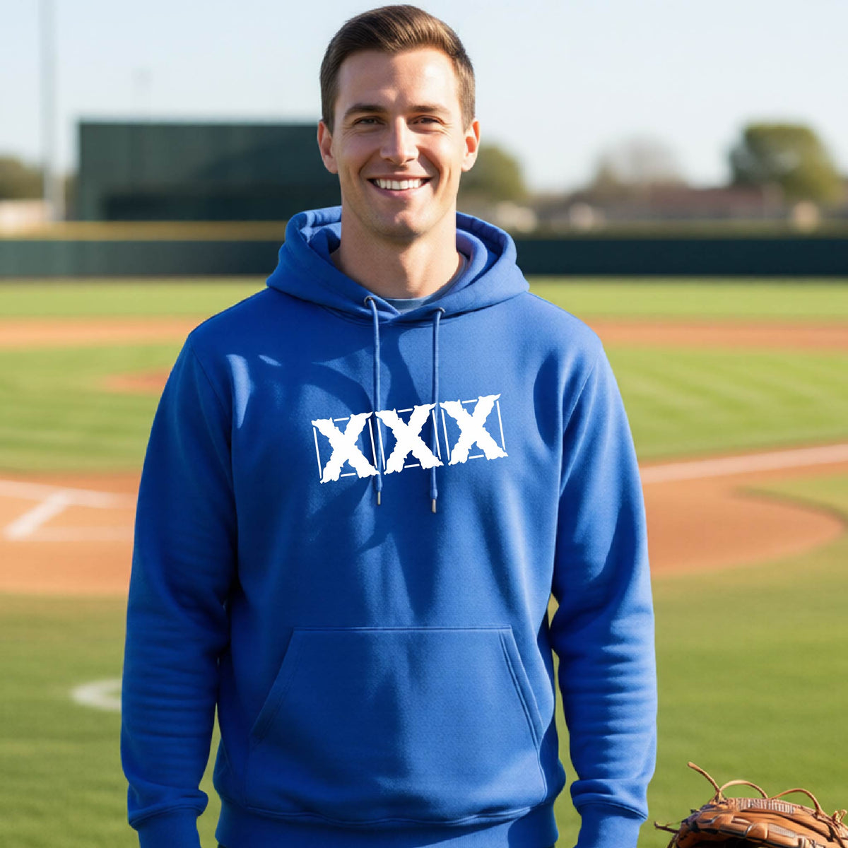 A smiling man wearing a royal blue hoodie with a white XXX logo on the chest, standing on a baseball field with a glove visible at the bottom right.