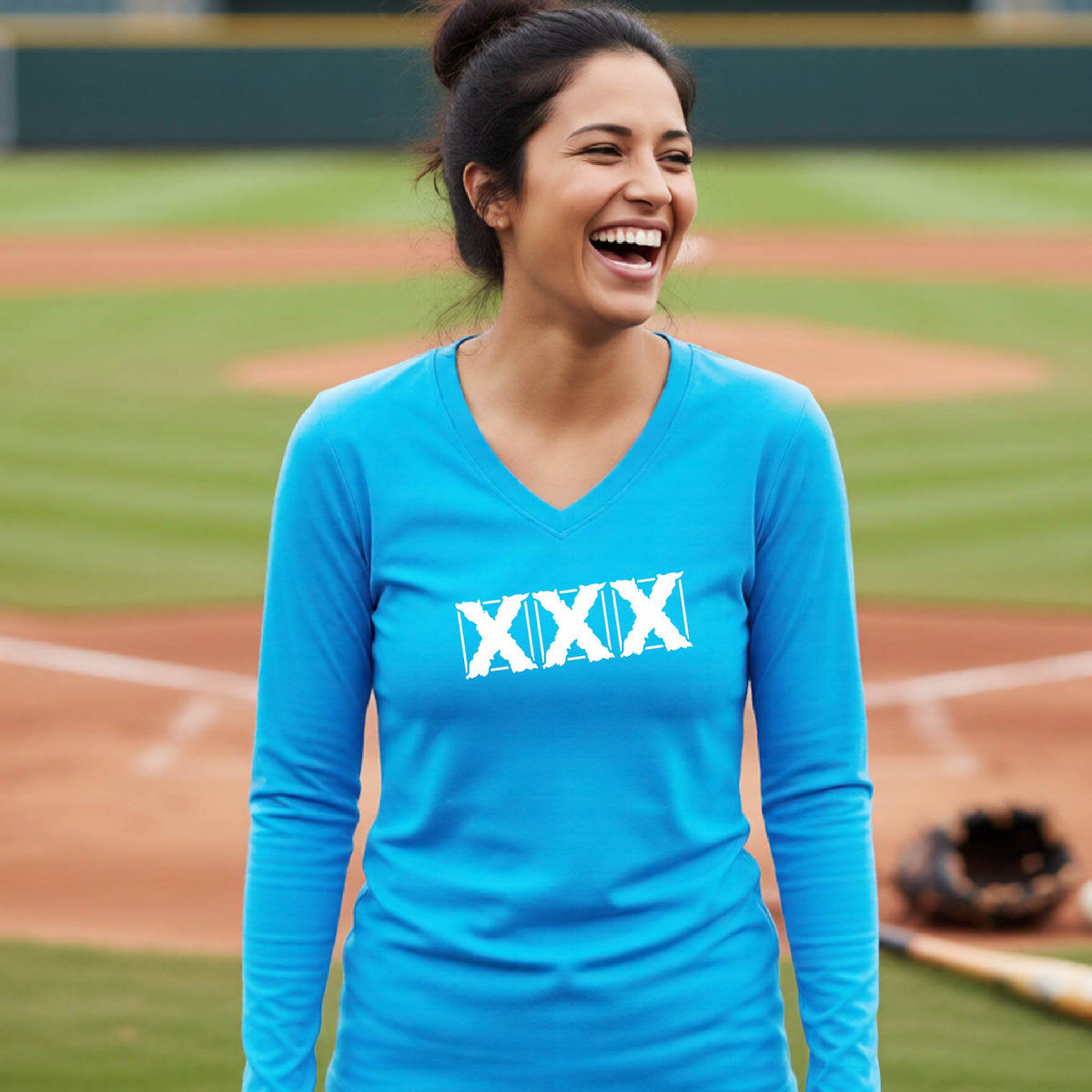 A woman smiling on a baseball field wearing a bright blue long-sleeve V-neck shirt with a white XXX logo across the chest.