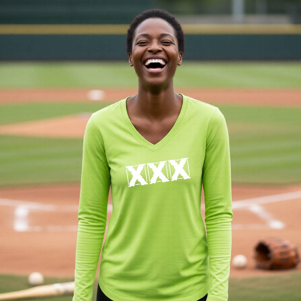 A woman laughing on a baseball field wearing a bright lime green long-sleeve V-neck shirt with a white 'XXX' graphic on the chest.
