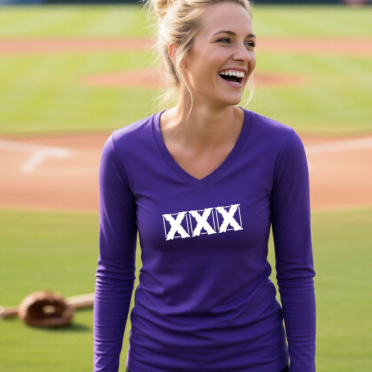 A woman laughing on a baseball field wearing a purple long-sleeve V-neck shirt with a white XXX logo on the chest.