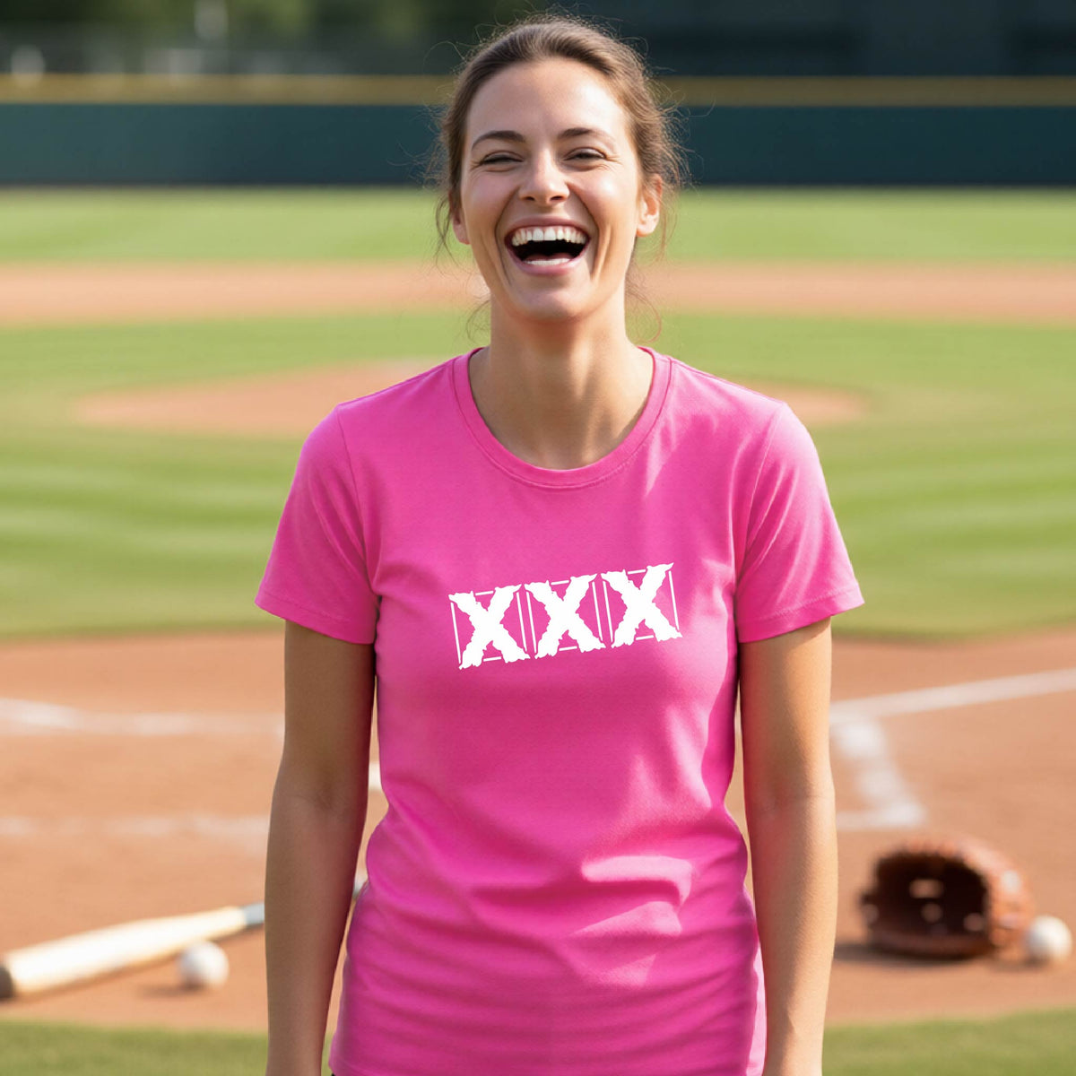 A woman laughing on a baseball field wearing a bright pink t-shirt with a white 'XXX' graphic across the chest.