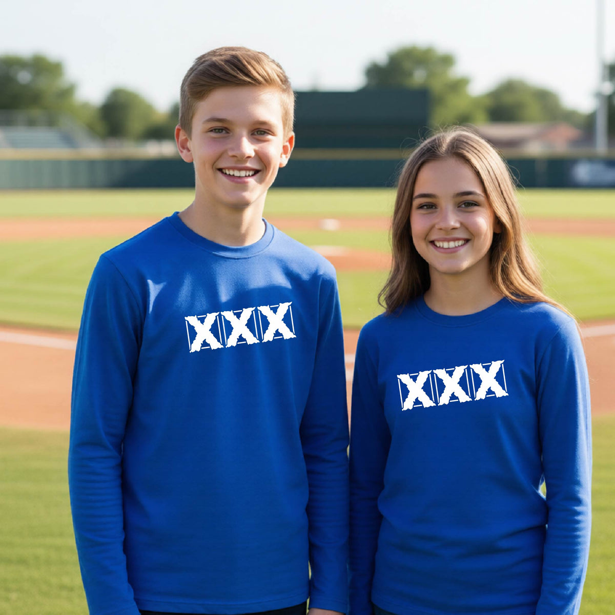 Two teenagers standing on a baseball field wearing matching royal long-sleeve shirts with a white letter logo 'XXX' graphic across the chest.