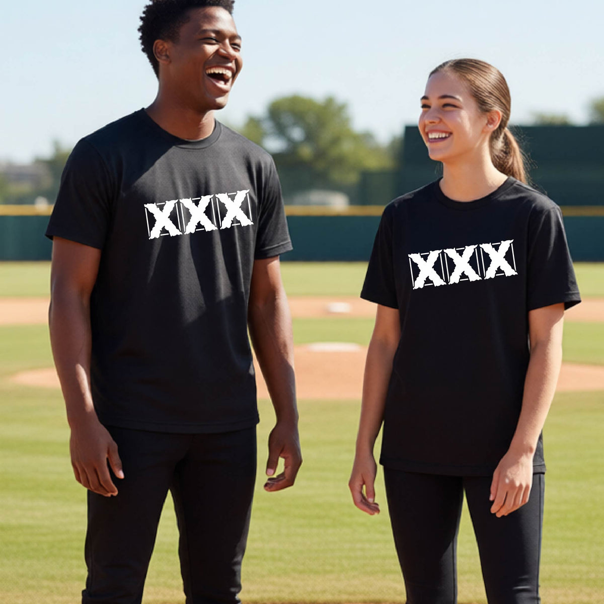 Two teenagers standing on a baseball field wearing matching black short-sleeve shirts with a white letter logo 'XXX' graphic across the chest.