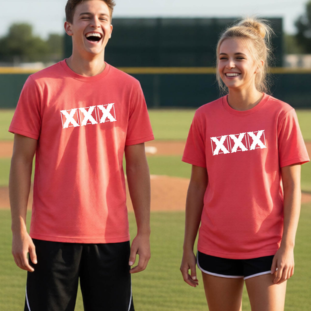 Two teenagers standing on a baseball field wearing matching coral colored short-sleeve shirts with a white letter logo 'XXX' graphic across the chest.