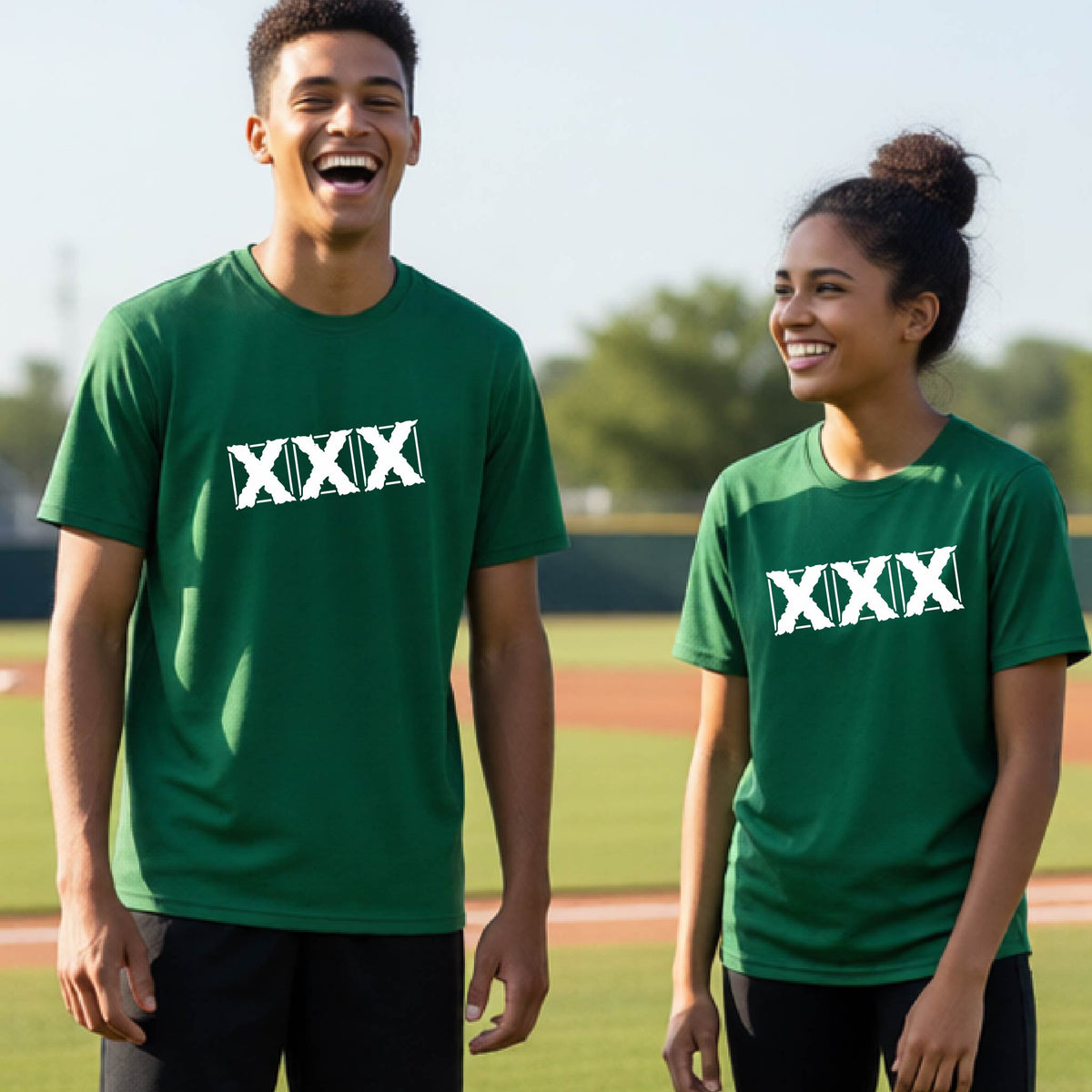 Two teenagers standing on a baseball field wearing matching green short-sleeve shirts with a white letter logo 'XXX' graphic across the chest.