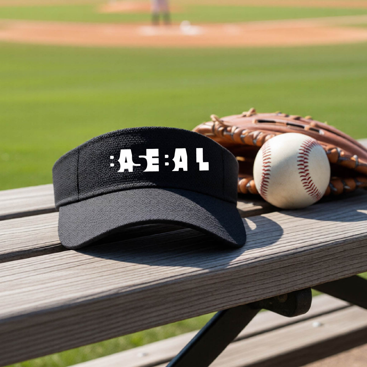A black baseball visor with white pixelated and cutout text reading 'BASEBALL' sits on a wooden baseball bench at a baseball field, with baseballs and a glove nearby.