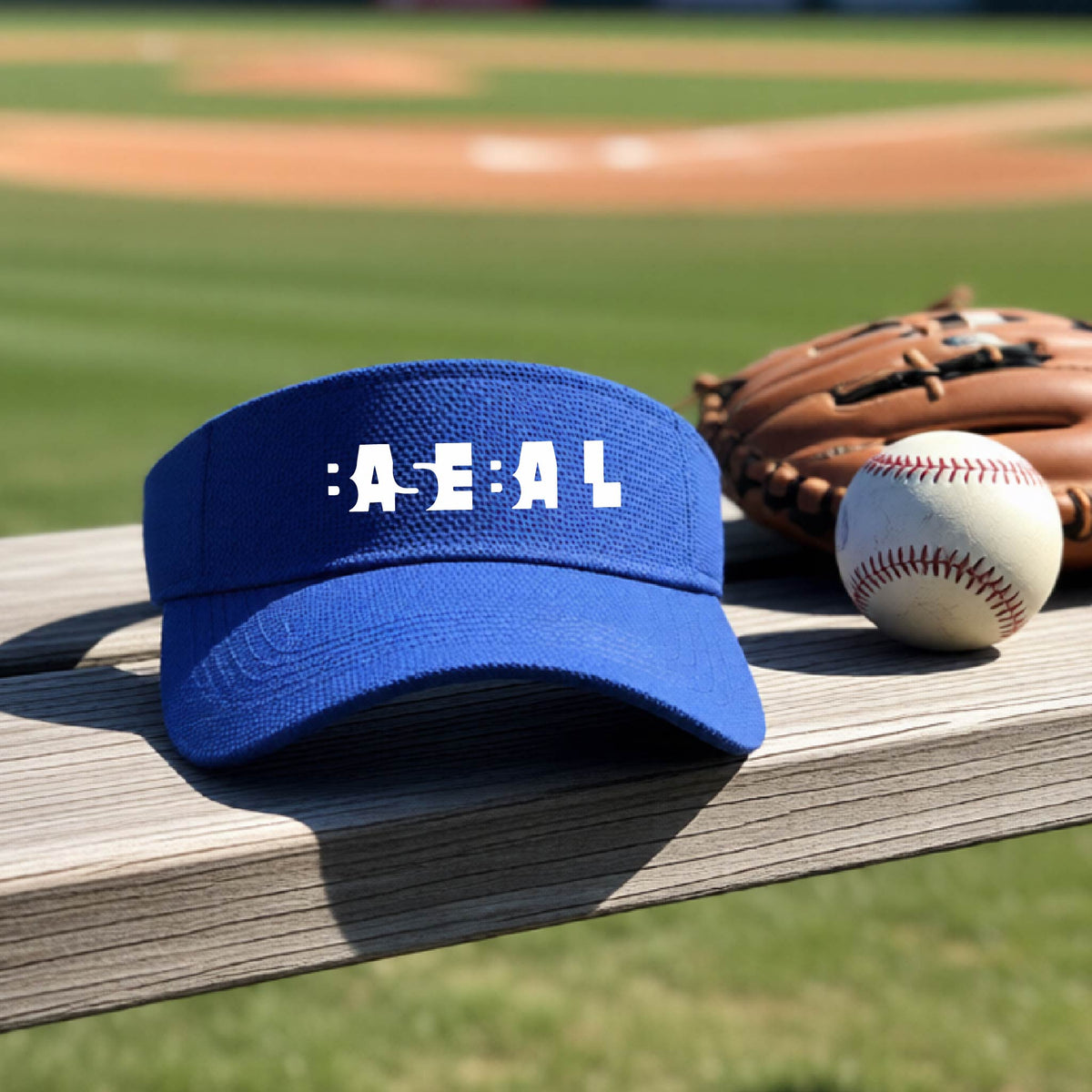 A royal blue baseball visor with white pixelated and cutout text reading 'BASEBALL' sits on a wooden baseball bench at a baseball field, with baseballs and a glove nearby.