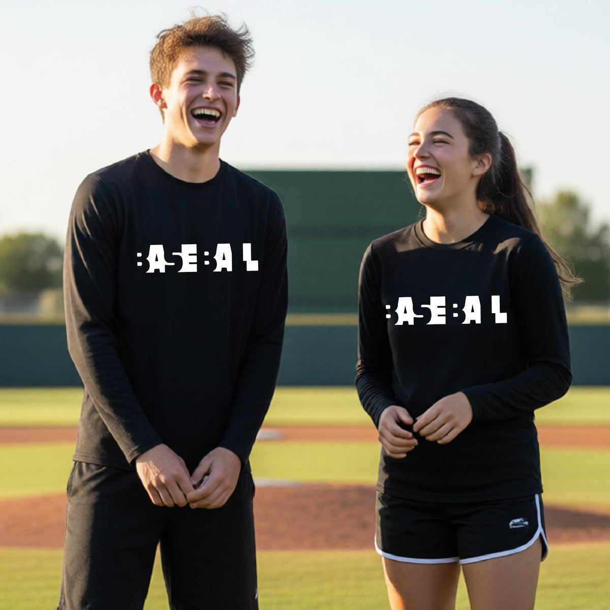 Two young athletes, standing on a baseball field wearing matching black long-sleeve t-shirts with white pixelated text that reads 'BASEBALL' in a cutout letter font.