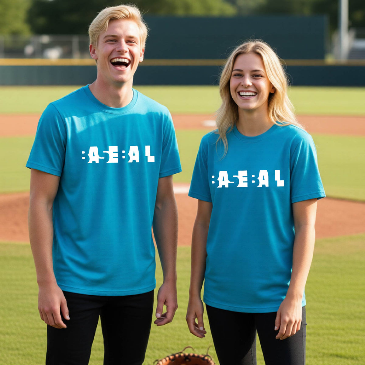 Two young people standing on a baseball field wearing matching bright blue t-shirts with the text 'BASEBALL' in a cutout artsy design printed in white across the chest.