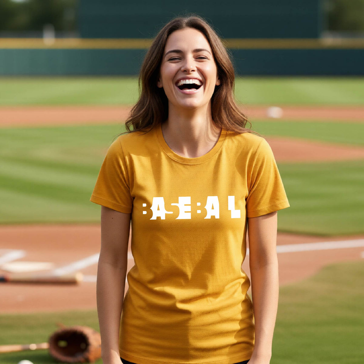 A smiling woman wearing a gold short-sleeve athletic shirt with the white text 'BASEBALL' in a cutout design printed across the chest, standing on a baseball field.