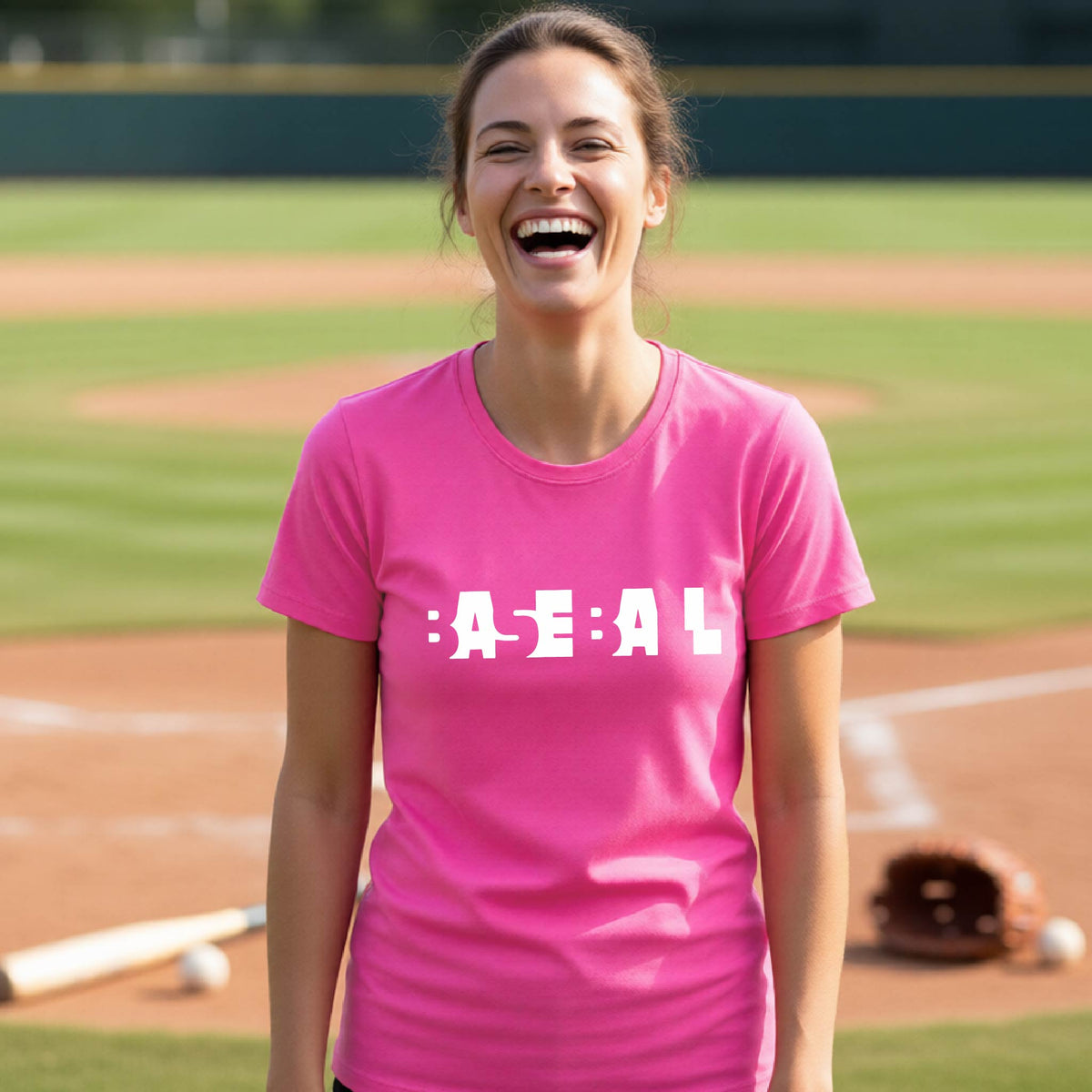 A smiling woman wearing a pink short-sleeve athletic shirt with the white text 'BASEBALL' in a cutout design printed across the chest, standing on a baseball field.