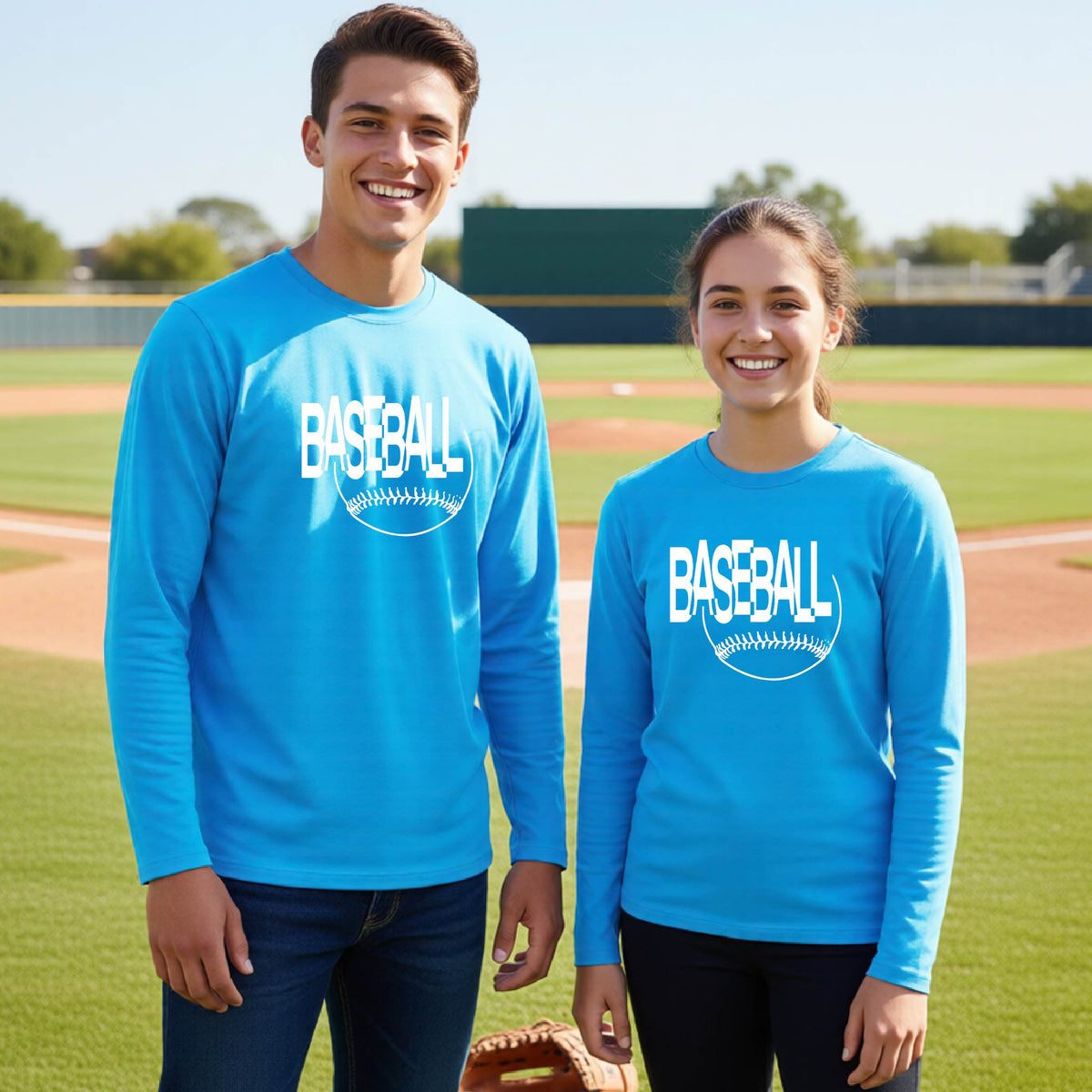 Two young athletes wearing matching bright blue long-sleeve t-shirts with a white baseball graphic on the chest stands on a baseball field. The shirt features the word 'BASEBALL' in a baseball-style font with a stitched ball design underneath.