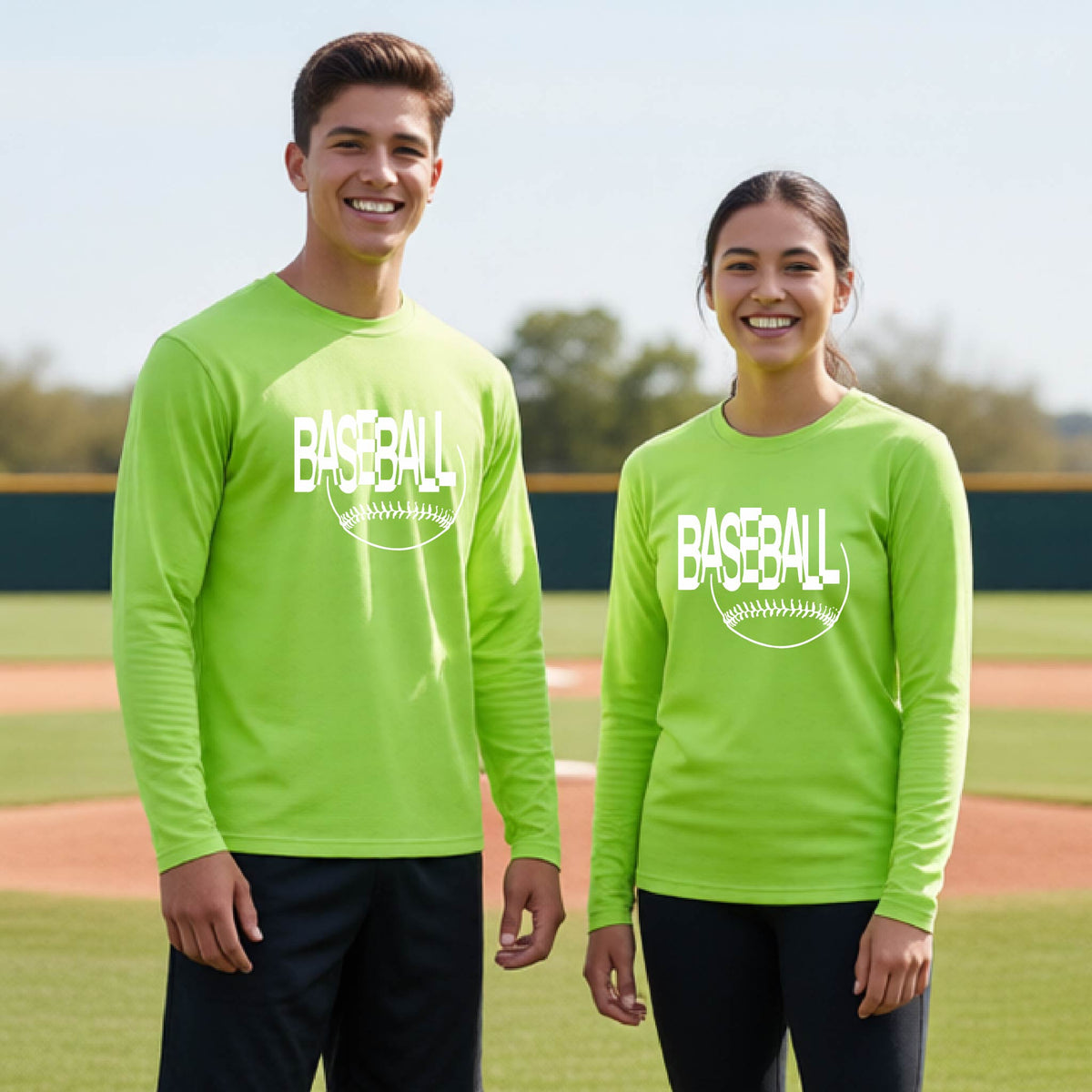 Two young athletes wearing matching lime green long-sleeve t-shirts with a white baseball graphic on the chest stands on a baseball field. The shirt features the word 'BASEBALL' in a baseball-style font with a stitched ball design underneath.