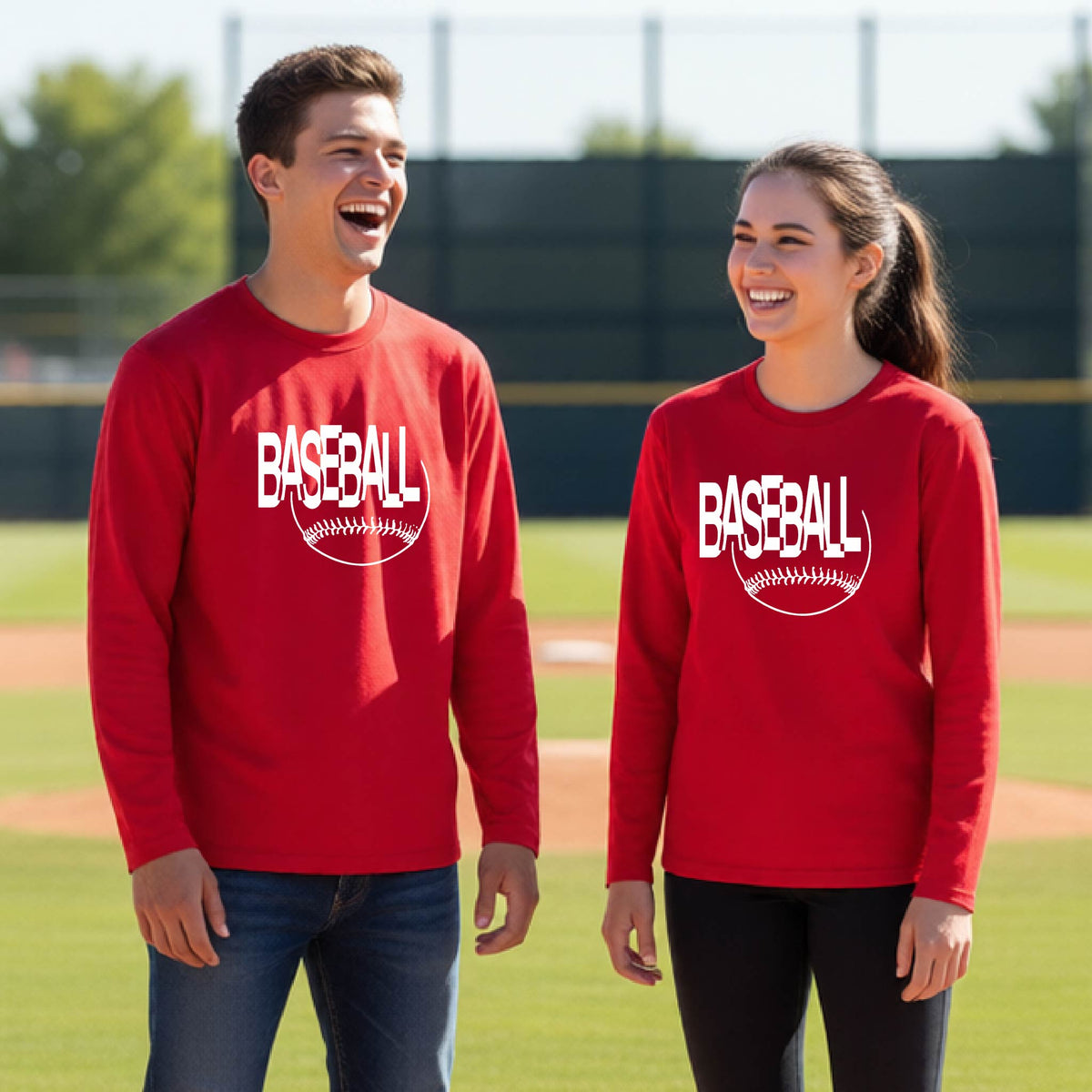 Two young athletes wearing matching red long-sleeve t-shirts with a white baseball graphic on the chest stands on a baseball field. The shirt features the word 'BASEBALL' in a baseball-style font with a stitched ball design underneath.