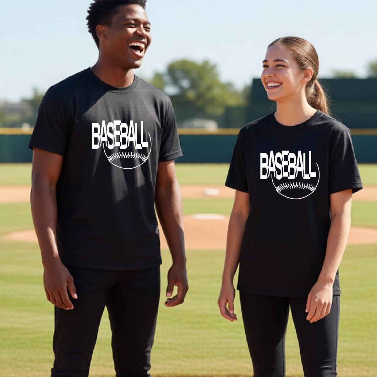 Two young athletes wearing matching black short-sleeve t-shirts with a white baseball graphic on the chest stands on a baseball field. The shirt features the word 'BASEBALL' in a baseball-style font with a stitched ball design underneath.