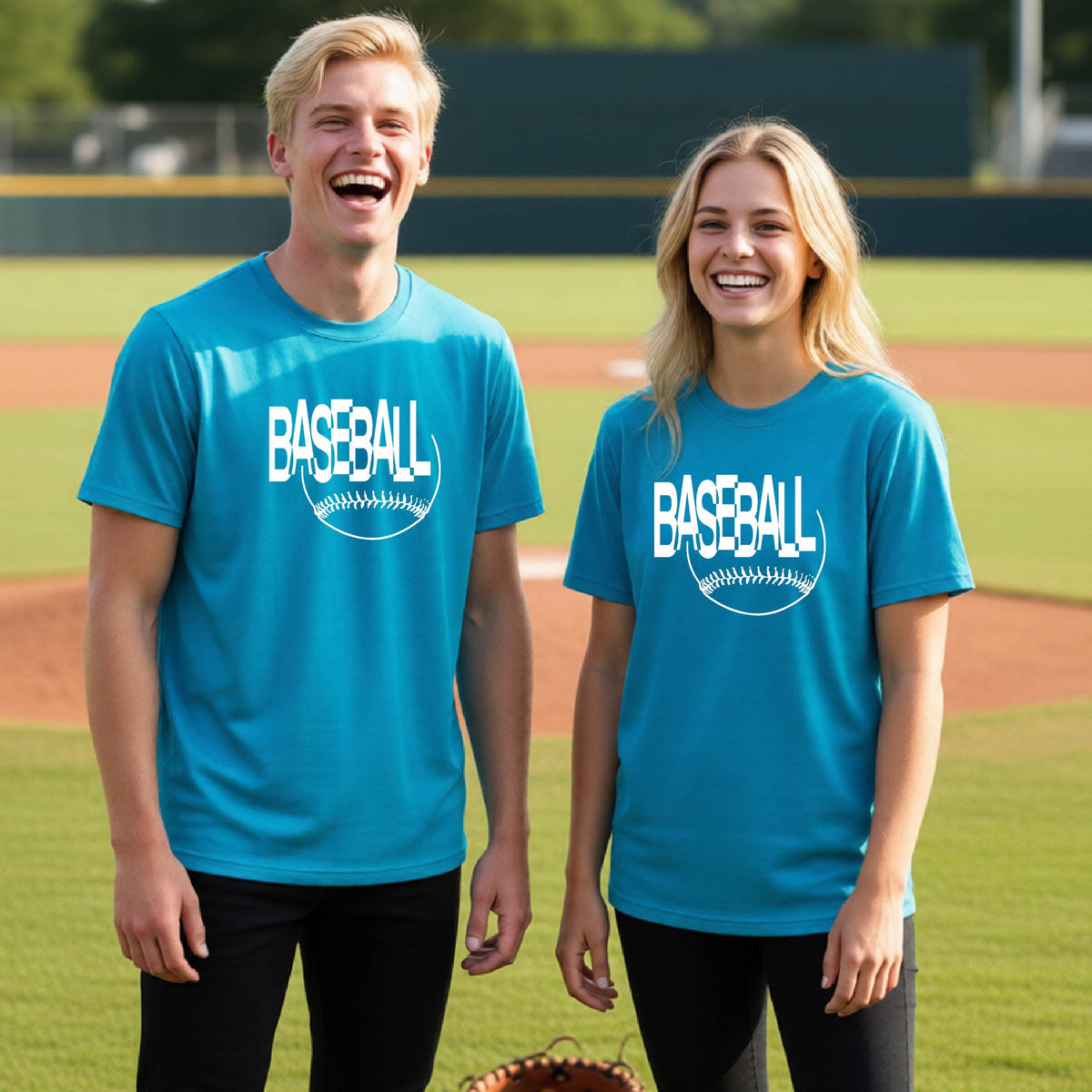 Two young athletes wearing matching bright blue short-sleeve t-shirts with a white baseball graphic on the chest stands on a baseball field. The shirt features the word 'BASEBALL' in a baseball-style font with a stitched ball design underneath.