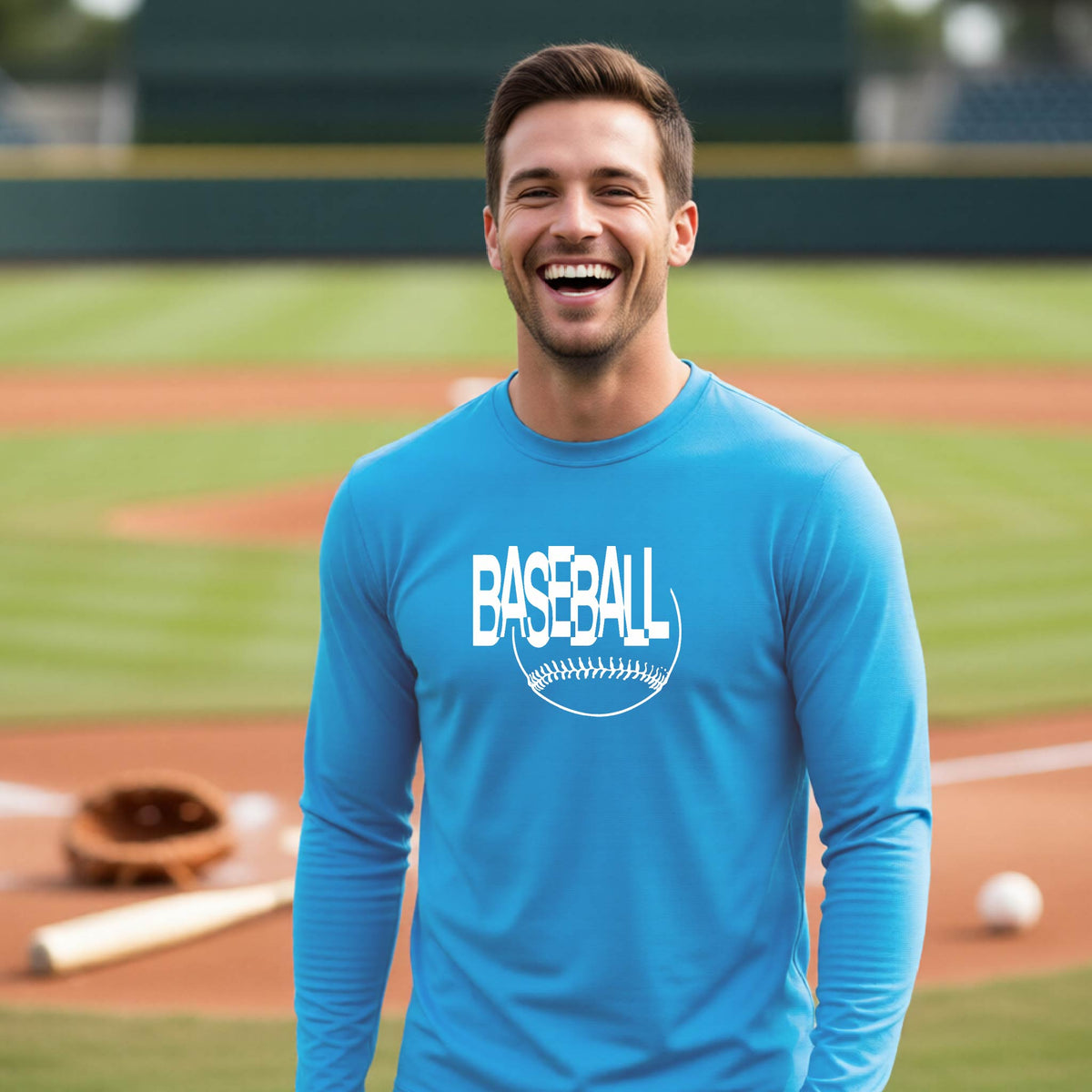 A man laughing on a baseball field wearing a bright blue long-sleeve t-shirt with a white 'BASEBALL' graphic and baseball stitching design on the front, standing on a baseball field.