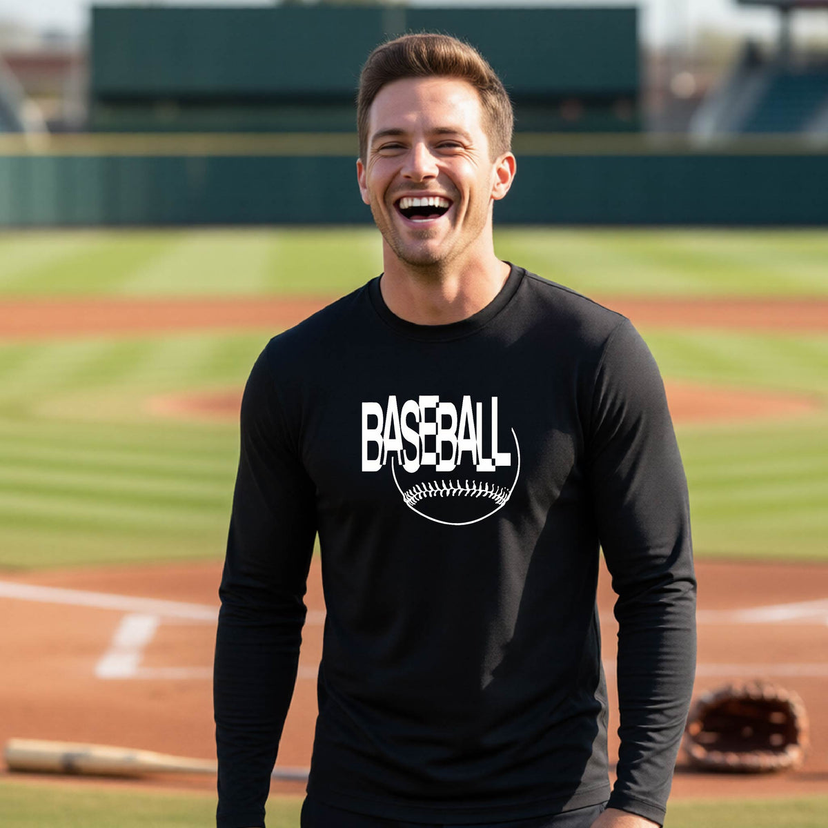 A man laughing on a baseball field wearing a black long-sleeve t-shirt with a white 'BASEBALL' graphic and baseball stitching design on the front, standing on a baseball field.