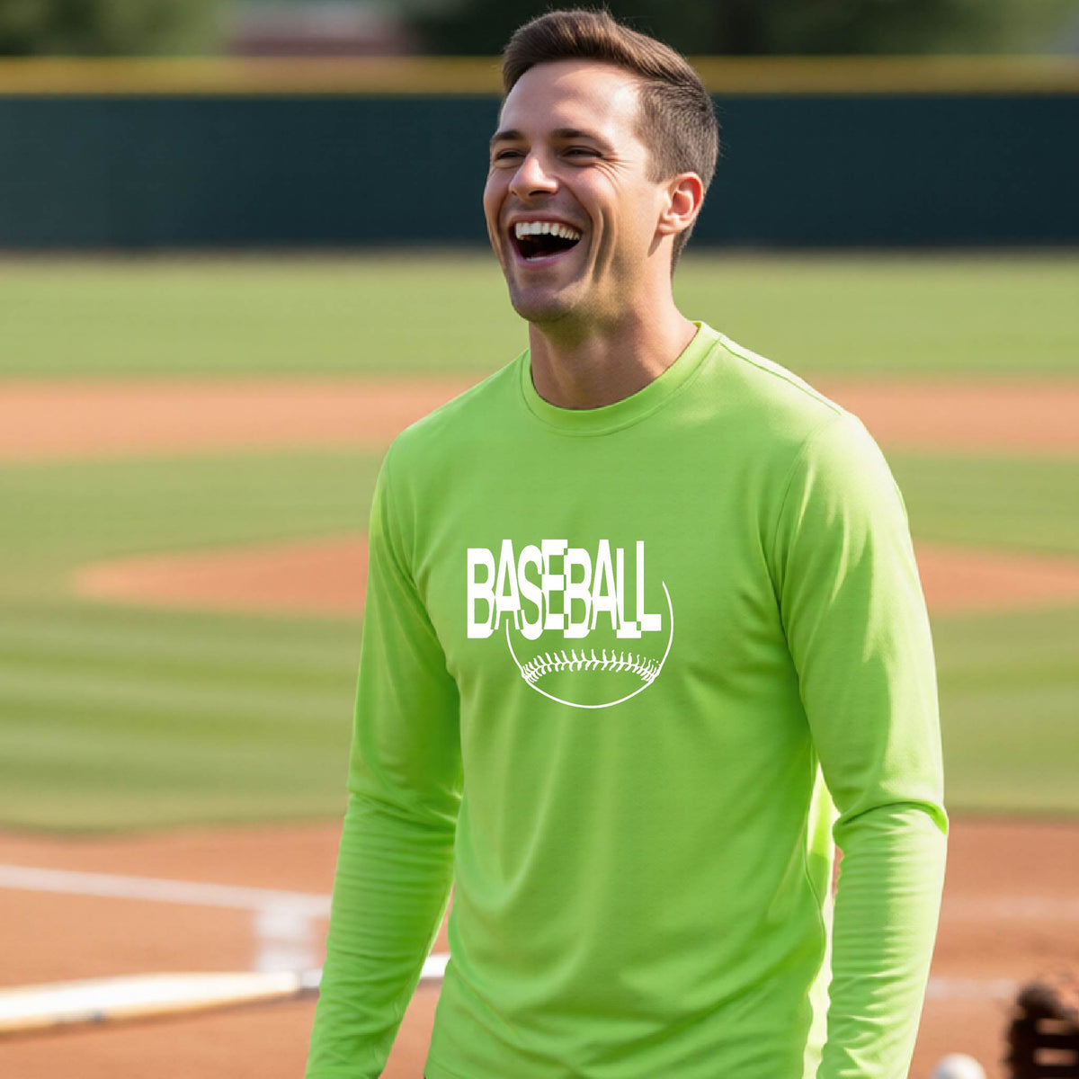 A man laughing on a baseball field wearing a bright lime green long-sleeve t-shirt with a white 'BASEBALL' graphic and baseball stitching design on the front, standing on a baseball field.