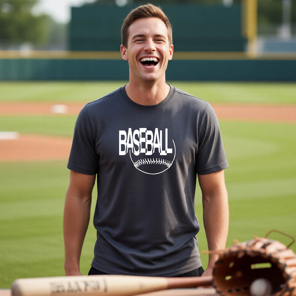 A man laughing on a baseball field wearing a dark gray t-shirt with a white 'BASEBALL' graphic and baseball stitching design on the chest.