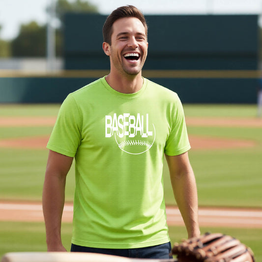 A man laughing on a baseball field wearing a bright lime green t-shirt with a white 'BASEBALL' graphic with a sketched ball underneath, with the baseball field blurred in the background.
