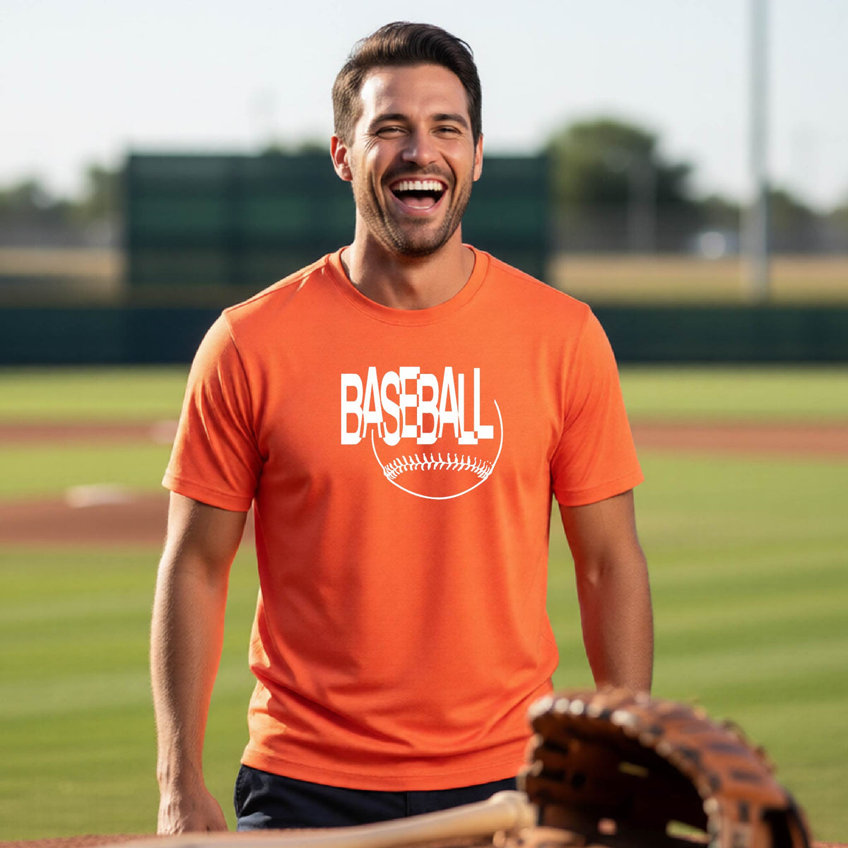 A man smiling on a baseball field wearing an orange t-shirt with a white 'BASEBALL' graphic and a baseball outline on the chest.