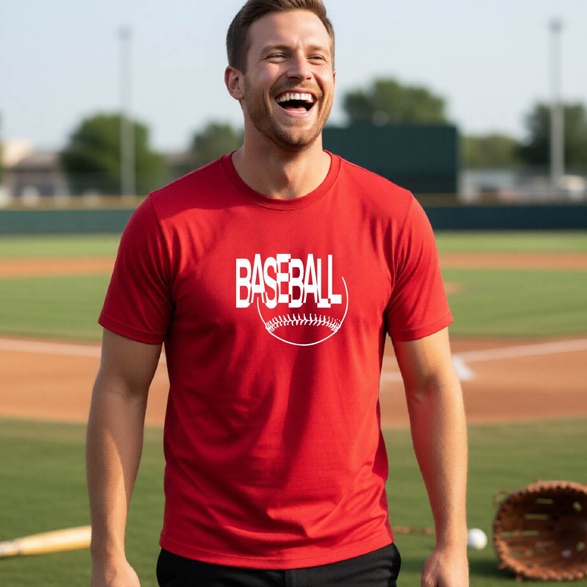 A man laughing on a baseball field wearing a red t-shirt with a white 'BASEBALL' graphic and baseball stitching design on the front.