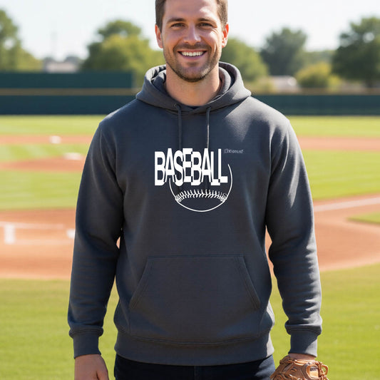 A smiling man wearing a dark gray hoodie with a white baseball graphic on the chest stands on a baseball field. The hoodie features the word 'BASEBALL' in a baseball-style font with a stitched ball design underneath.