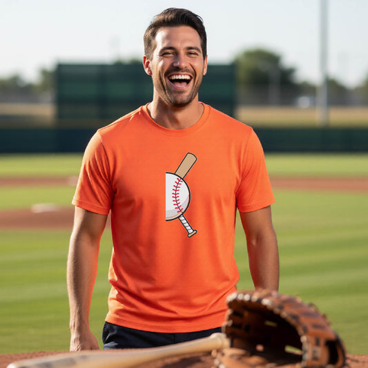 A man smiling in front of a baseball diamond wearing an orange short-sleeve t-shirt, with a colorful graphic of a half baseball with a curved bat behind it, printed on the front of the shirt. 