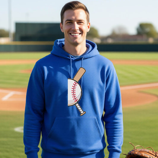 A man smiling in front of a baseball diamond wearing a royal blue hoodie pullover, with a colorful graphic of a half baseball with a curved bat behind it, printed on the front of the shirt. 