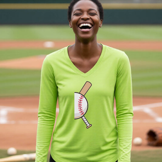 A woman smiling in front of a baseball diamond wearing a lime green long-sleeve t-shirt, with a colorful graphic of a half baseball with a curved bat behind it, printed on the front of the shirt. 