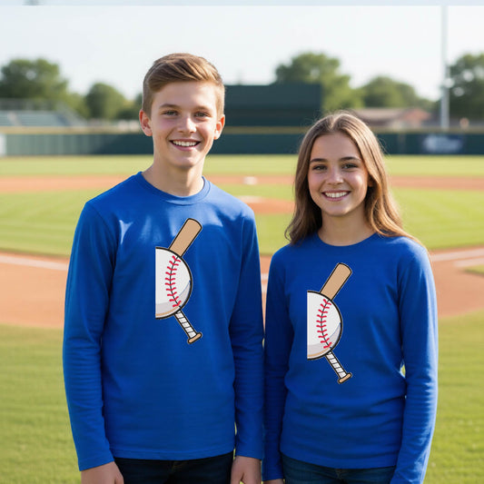 Two youth athletes wearing matching shirts, smiling in front of a baseball diamond wearing royal blue long-sleeve t-shirts, with a colorful graphic of a half baseball with a curved bat behind it, printed on the front of the shirt. 