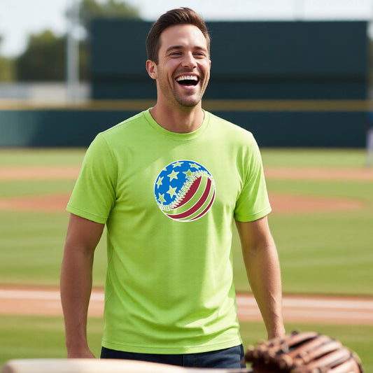 A man smiling in front of a baseball diamond wearing a lime green short-sleeve t-shirt with a colored graphic of an American flag patriotic baseball with stars and stripes printed on the front.