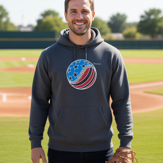 A man smiling in front of a baseball diamond wearing a dark gray hoodie pullover with a colored graphic of an American flag patriotic baseball with stars and stripes printed on the front.
