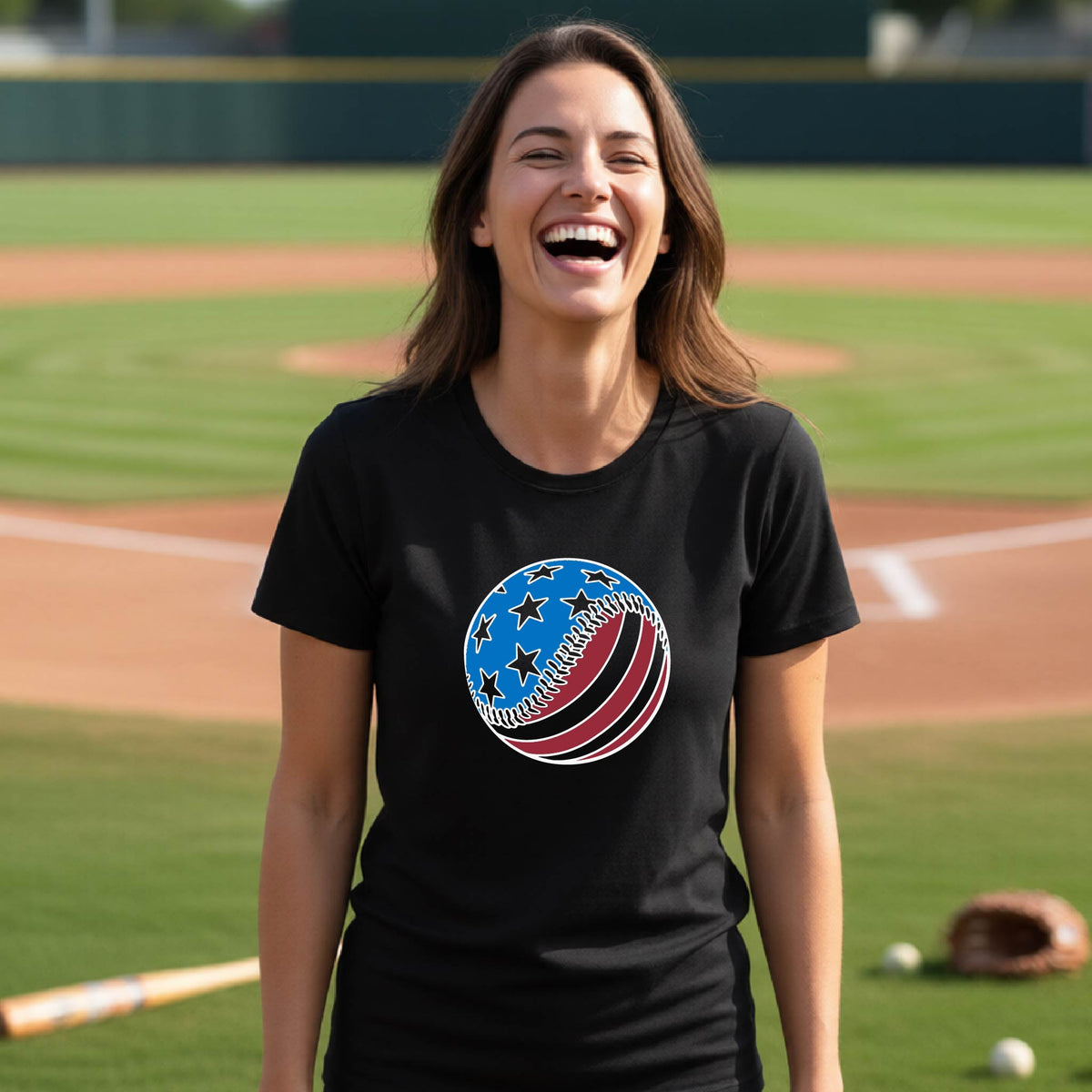 A woman smiling in front of a baseball diamond wearing a black t-shirt with a colored graphic of an American flag patriotic baseball with stars and stripes printed on the front.