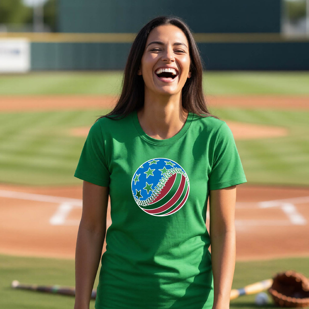 A woman smiling in front of a baseball diamond wearing a green t-shirt with a colored graphic of an American flag patriotic baseball with stars and stripes printed on the front.