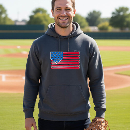 A man smiling in front of a baseball diamond wearing a dark gray hoodie pullover with a colored graphic of an American flag using baseball bats and balls and a home plate, printed on the front.