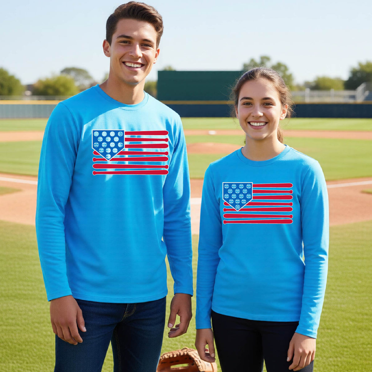 Two young athletes wearing matching shirts smiling in front of a baseball diamond wearing bright blue long-sleeve t-shirts with a colored graphic of an American flag using baseball bats and balls and a home plate, printed on the front.