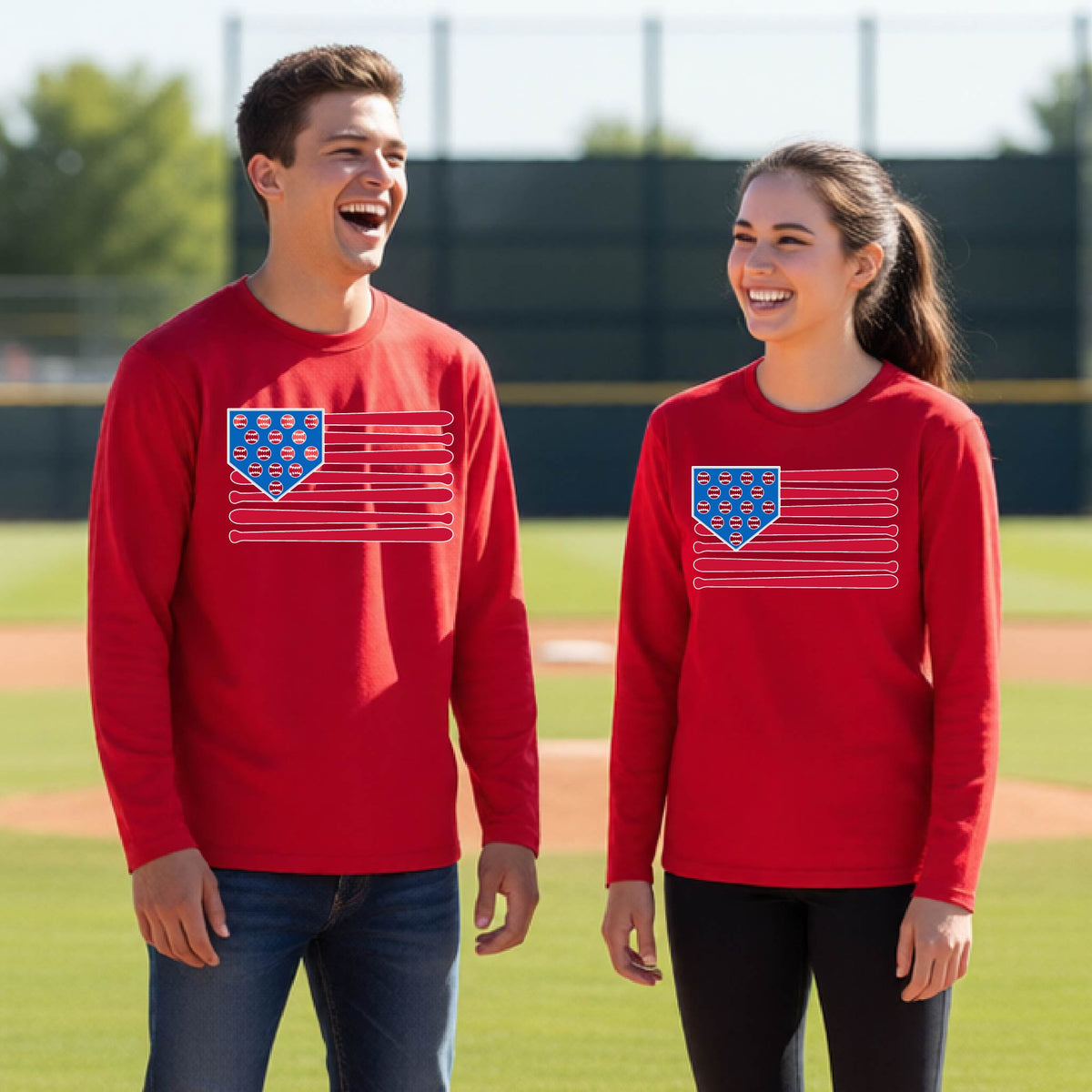Two young athletes wearing matching shirts smiling in front of a baseball diamond wearing red long-sleeve t-shirts with a colored graphic of an American flag using baseball bats and balls and a home plate, printed on the front.
