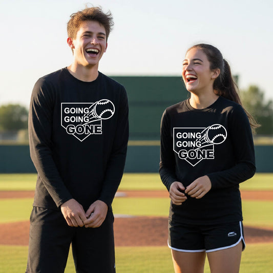 Two youth athletes wearing matching black long-sleeve t-shirts, smiling in front of a baseball diamond, with a white graphic of a baseball in flight in front of a home plate with the words ‘GOING GOING GONE’, printed on the front of the shirt.