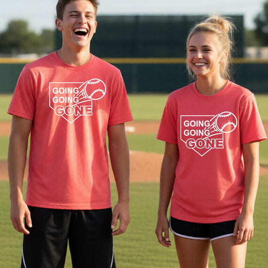 Two youth athletes wearing matching coral pink short-sleeve t-shirts, smiling in front of a baseball diamond, with a white graphic of a baseball in flight in front of a home plate with the words ‘GOING GOING GONE’, printed on the front of the shirt.