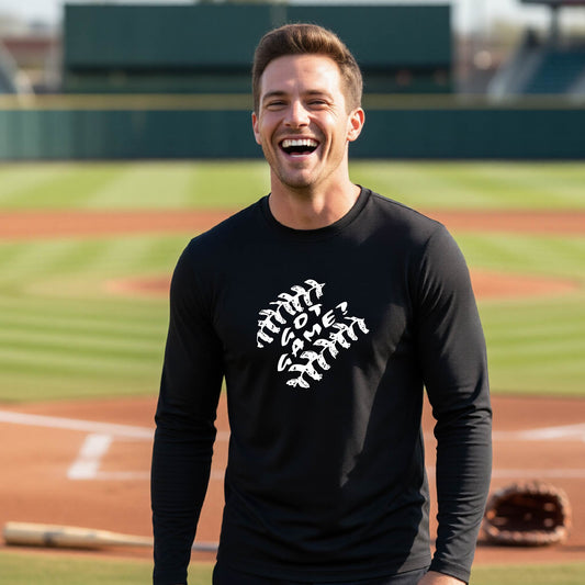 A man smiling in front of a baseball diamond wearing a black long-sleeve t-shirt, with a white graphic of baseball stitches and the words ‘GOT GAME’ inside, printed on the front of the shirt.