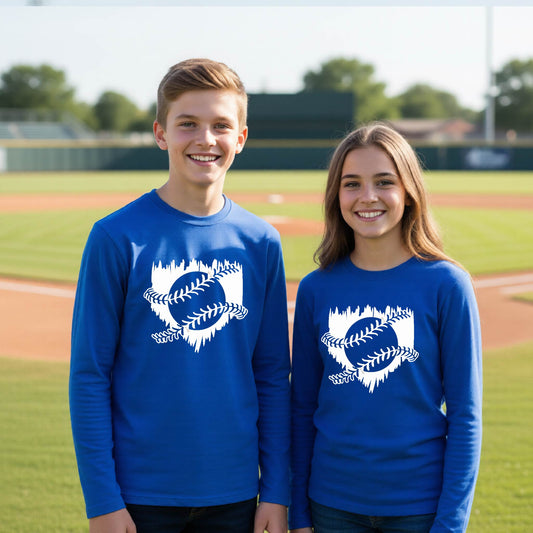 Two youth athletes wearing matching royal blue long-sleeve t-shirts, smiling in front of a baseball diamond, with an artistic white graphic of a sketch of baseball home plate with baseball stitches across the front, printed on the front of the shirt.