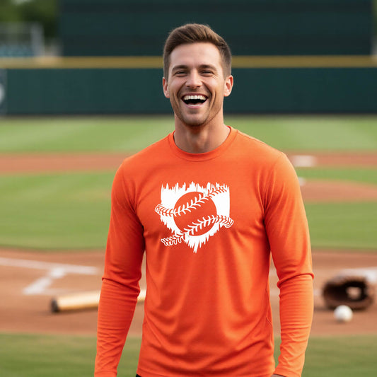 A man smiling in front of a baseball diamond wearing an orange long-sleeve t-shirt, with an artistic white graphic of a sketch of baseball home plate with baseball stitches across the front, printed on the front of the shirt.