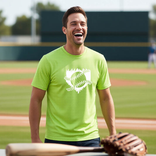 A man smiling in front of a baseball diamond wearing a ;lime green short-sleeve t-shirt, with an artistic white graphic of a sketch of baseball home plate with baseball stitches across the front, printed on the front of the shirt.