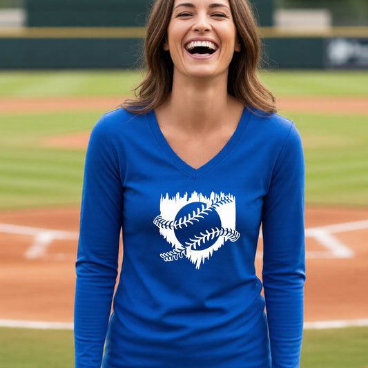 A woman smiling in front of a baseball diamond wearing a royal blue long-sleeve t-shirt, with an artistic white graphic of a sketch of baseball home plate with baseball stitches across the front, printed on the front of the shirt.
