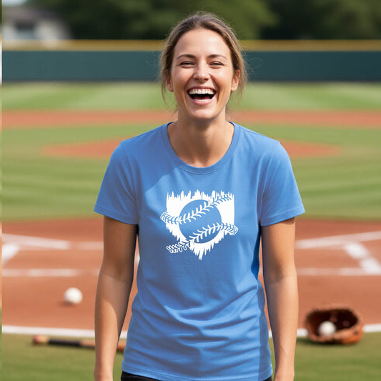 A woman smiling in front of a baseball diamond wearing a blue short-sleeve t-shirt, with an artistic white graphic of a sketch of baseball home plate with baseball stitches across the front, printed on the front of the shirt.